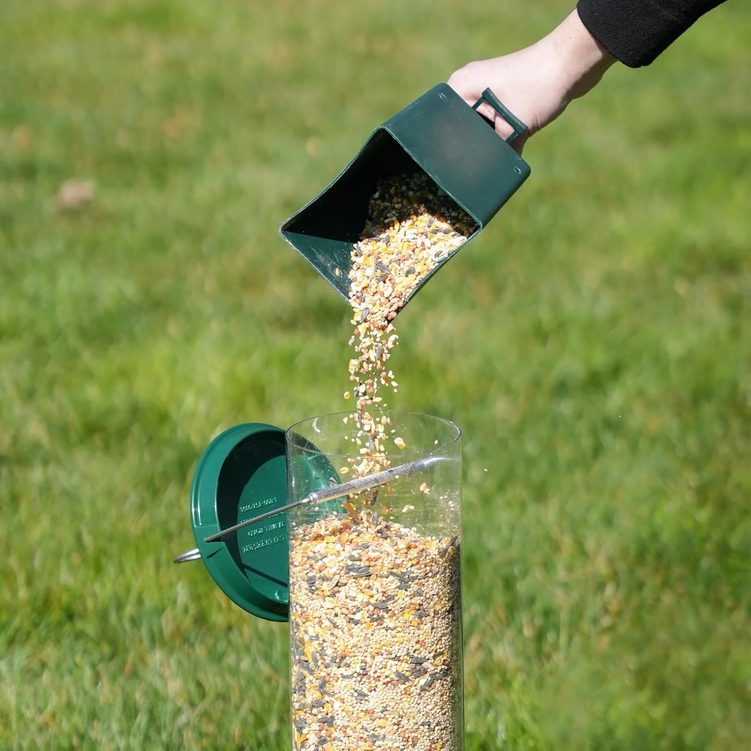 Refilling a squirrel proof wild bird feeder with mixed bird seed outdoors
